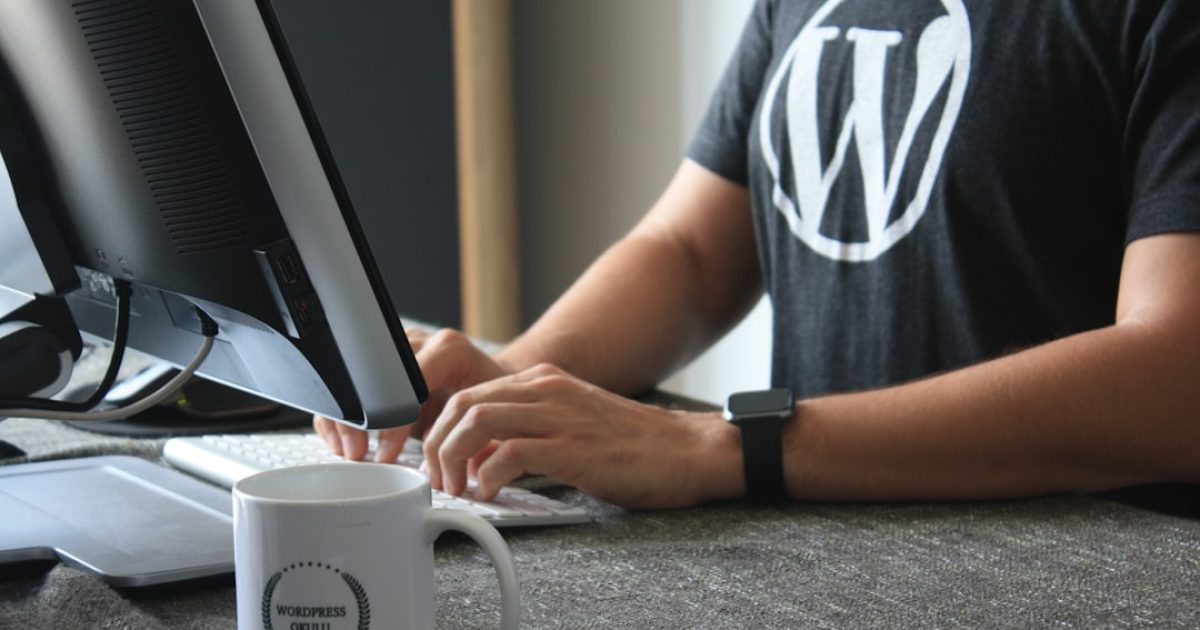 Mãos de pessoa a trabalhar num portátil com o logótipo do WordPress no ecrã, simbolizando a gestão de atualizações de um site.