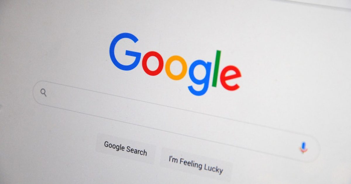 Mãos a trabalhar num portátil com o logótipo do Google no ecrã, gráficos de ranking de SEO e uma lupa, representando análise de dados e otimização.